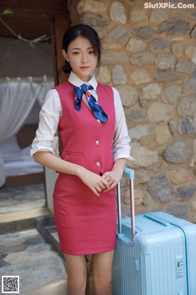 A woman in a pink dress with a blue suitcase.