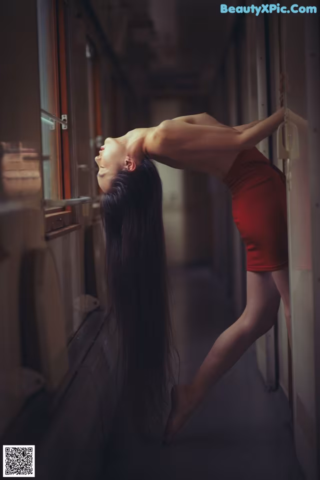 A woman in a red dress leaning against a window.