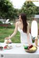 A woman in a white dress preparing food on a table.