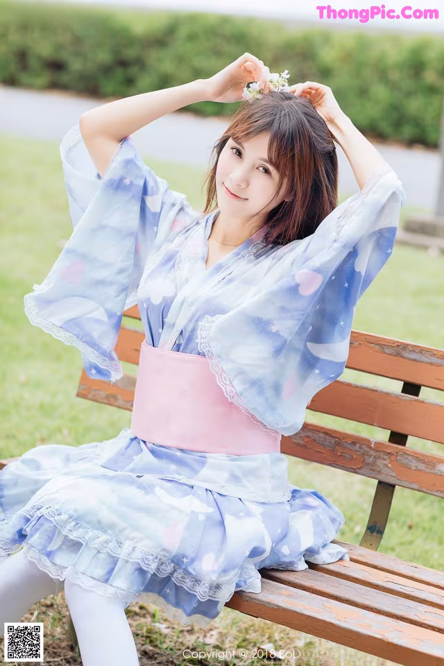 A woman in a blue and pink dress sitting on a bench.