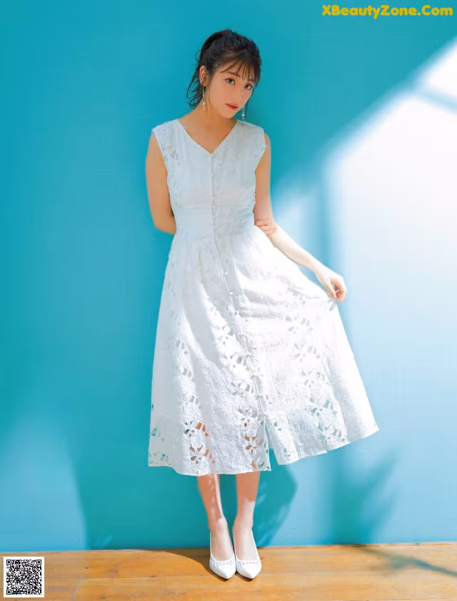 A woman in a white dress standing in front of a blue wall.