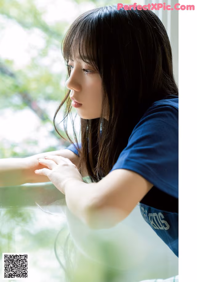 A young woman sitting at a table looking out a window.