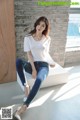 A woman sitting on a white bench wearing a white shirt and jeans.