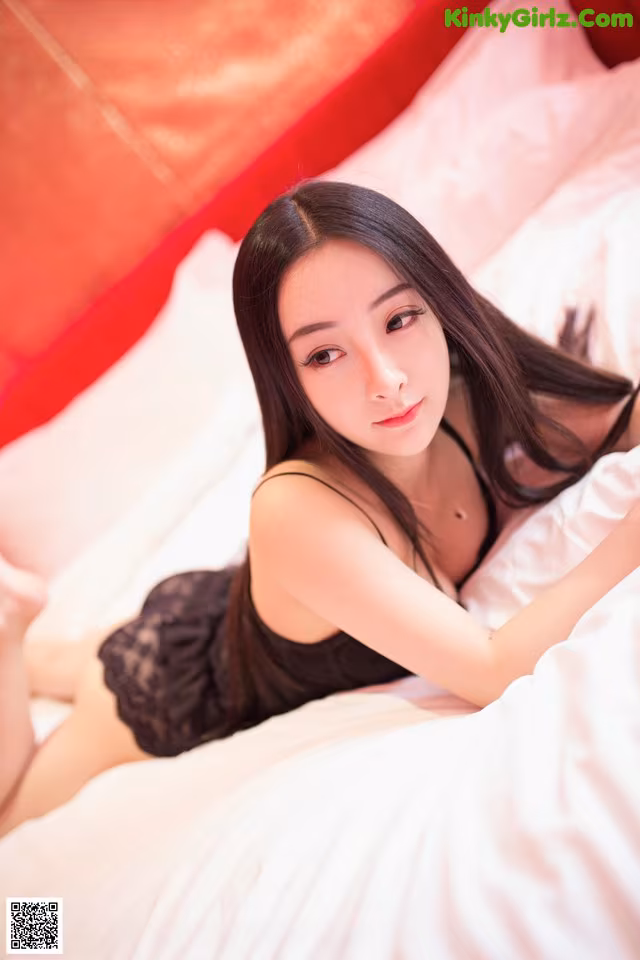 A woman laying on top of a bed in a black dress.
