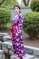 A woman in a purple kimono standing next to a pond.