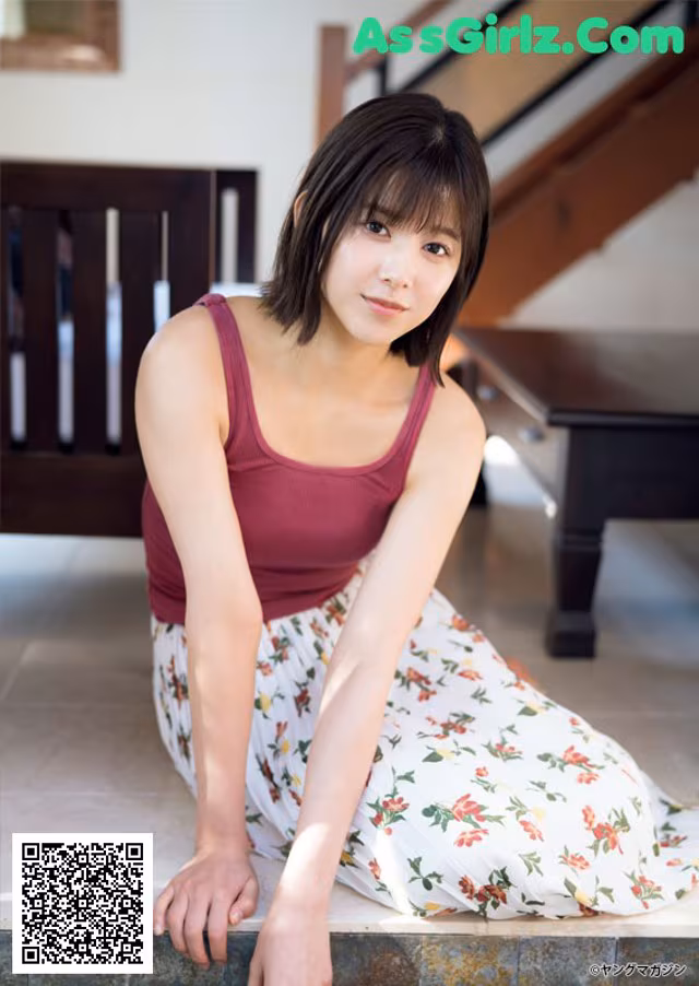 A woman in a red tank top and floral skirt sitting on the floor.