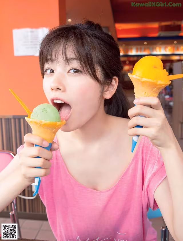 A young woman eating two ice cream cones in a restaurant.