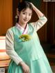 A woman in a green and white hanbok poses for a picture.