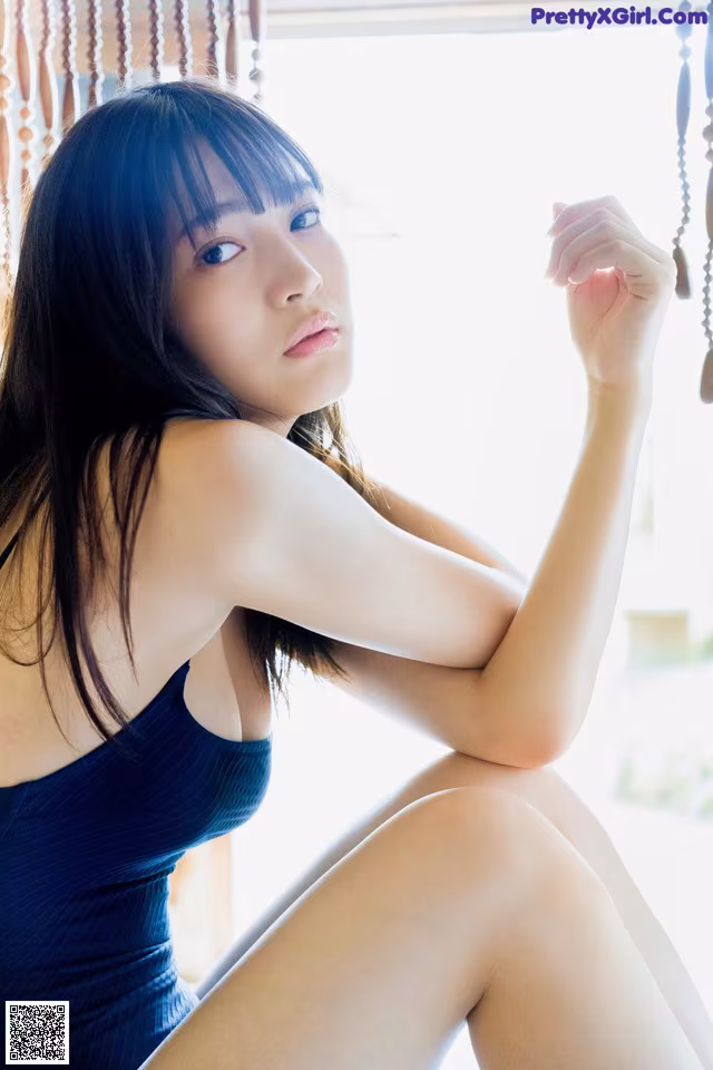 A woman in a blue dress sitting on a window sill.