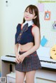 A woman in a school uniform posing in front of a piano.