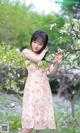 A woman in a floral dress standing in front of a tree.