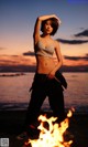 A woman standing in front of a fire on the beach.