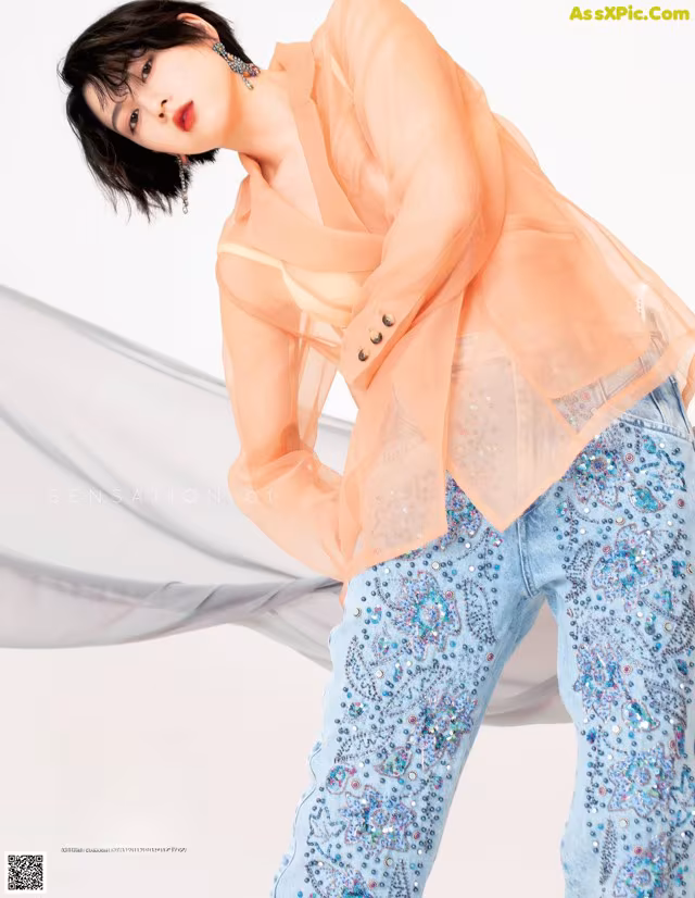 A woman in a sheer top and blue pants posing for a magazine.
