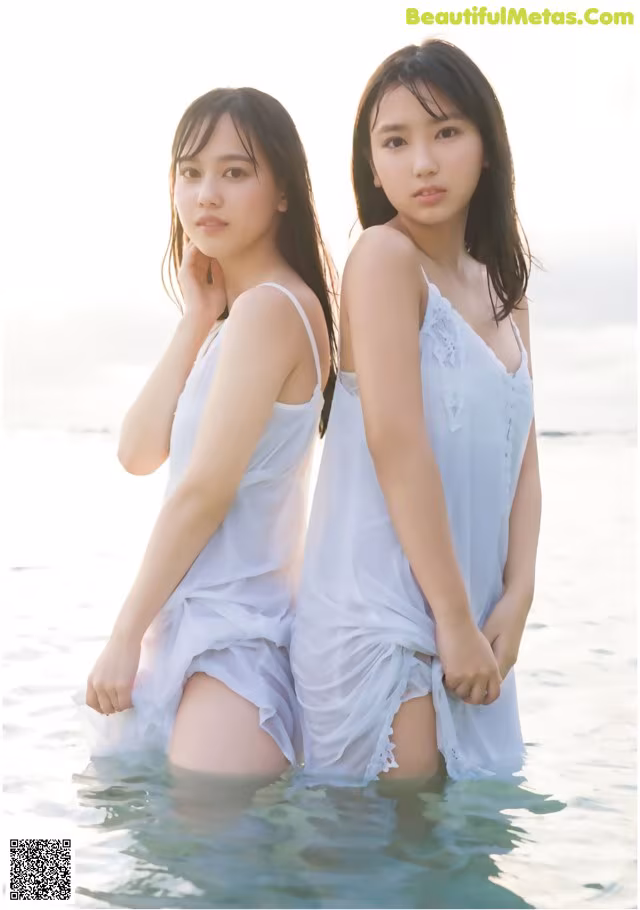 Two young women standing in the water wearing white dresses.