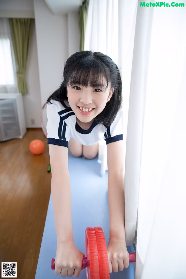 A young girl holding a red dumbbell on a blue mat.